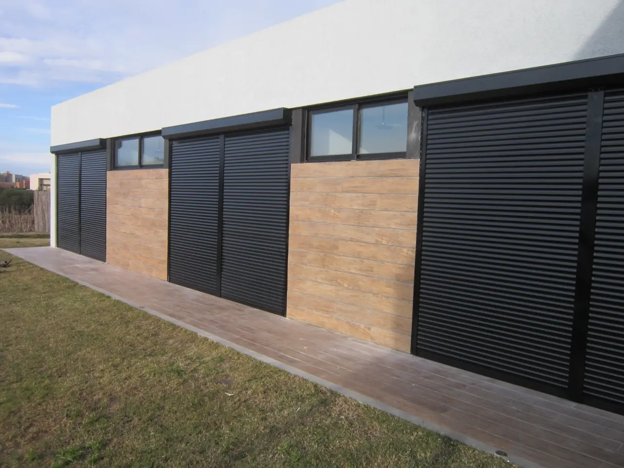 Cortinas de enrollar oscuras cerradas en los ventanales de una fachada con revestimiento de madera