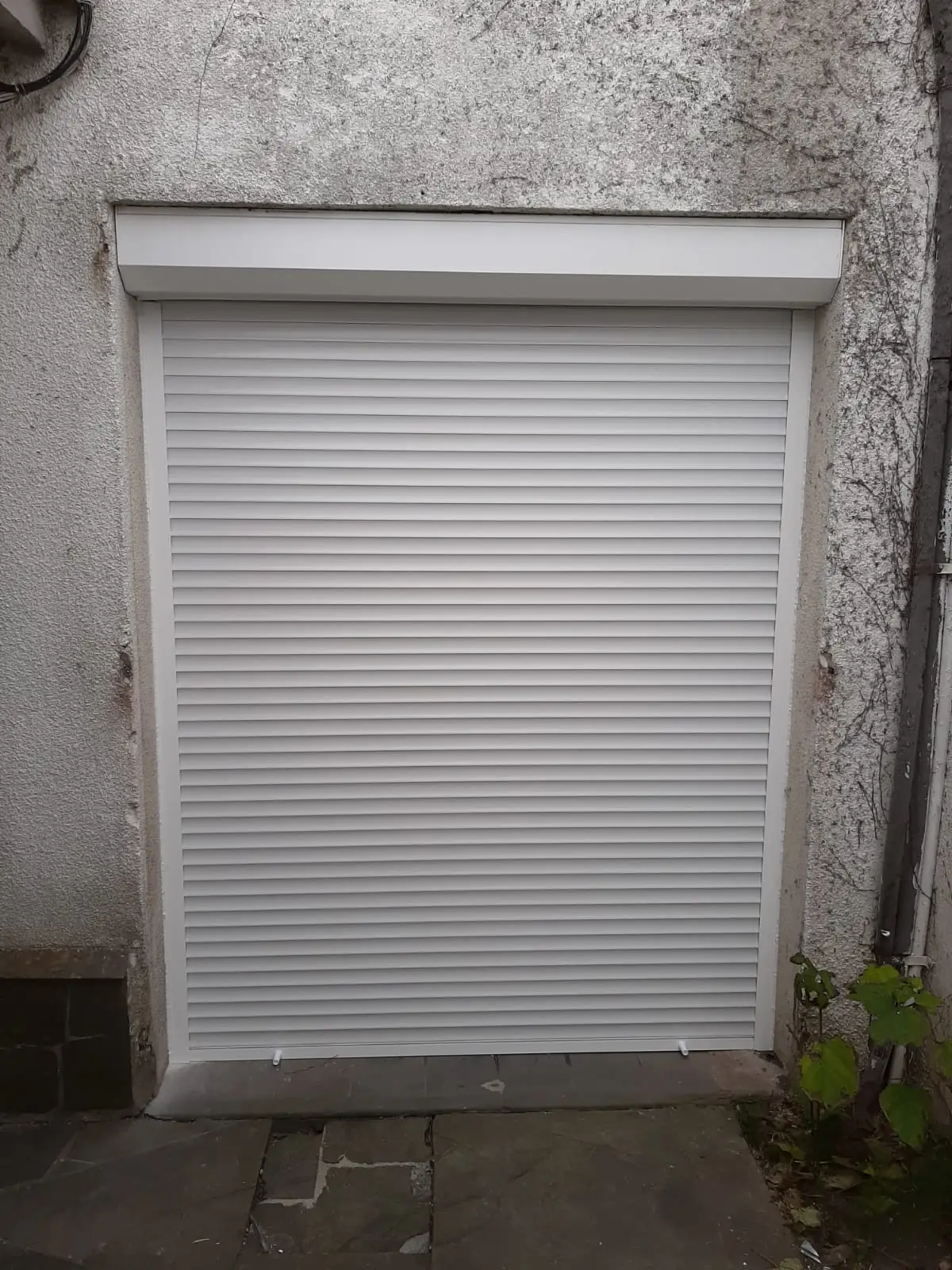 Cortina de enrollar blanca cerrada, con su cajón, en una puerta exterior