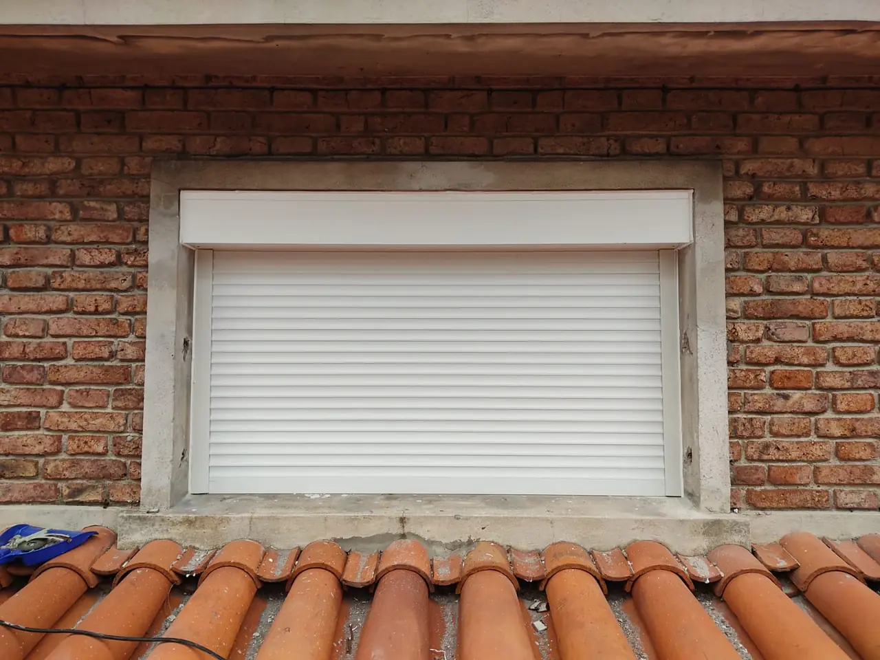 Cortina de enrollar blanca con cajón en una ventana sobre una pared de ladrillo