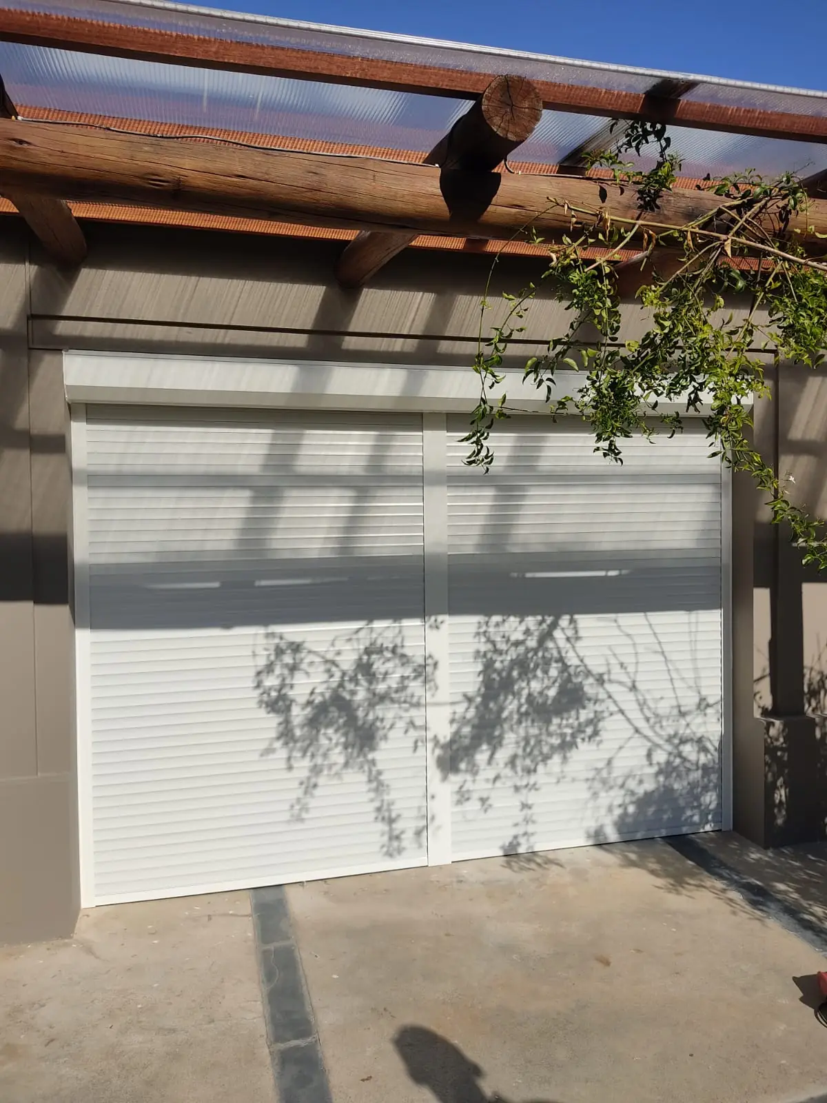 Cortina de enrollar blanca cerrada en una abertura bajo una pérgola