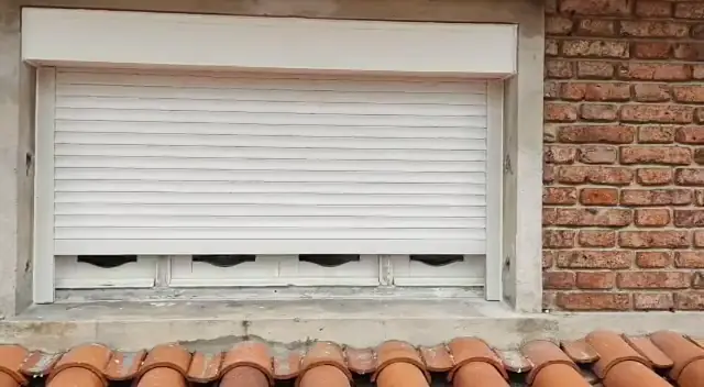Cortina de enrollar blanca subiendo en una ventana sobre una pared de ladrillo