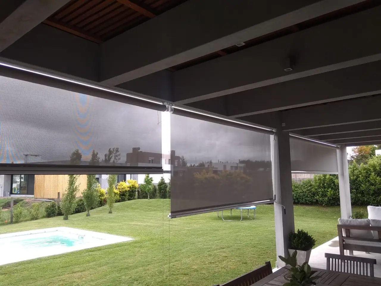 Toldo vertical de tela screen en una galería frente a una piscina