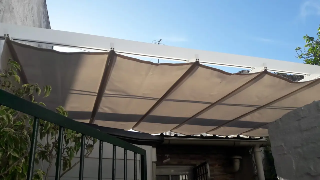 Toldo de lona plegado en ondas bajo una estructura de patio