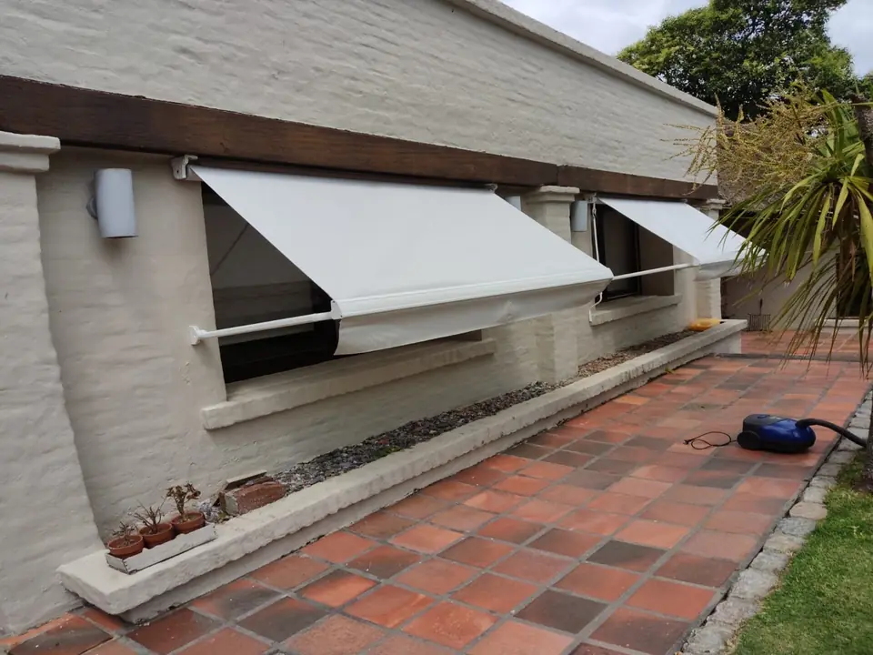Toldos de brazo sobre las ventanas de una casa con patio